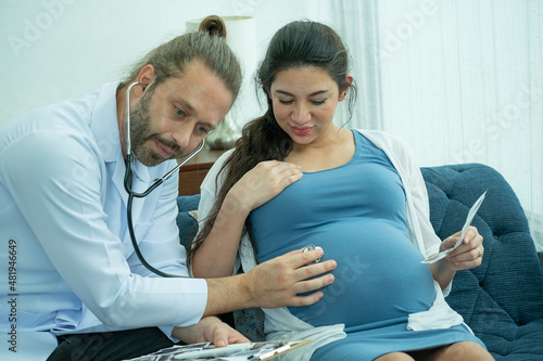 Doctor use stethtroscope to listen baby sound in belly of pregnant woman sit in living room at home. Concept of medicare for pregnant woman and support good health.