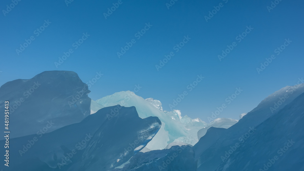 Fototapeta premium Ice hummocks against the sky. Close-up. The glare of the sun on the edges. Light and shadows. All shades of blue. Baikal. Copy space. Full screen