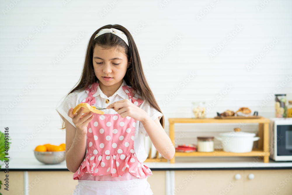 Young Caucasian girl wearing pajamas while put yam spread on the bread for breakfast inside of the modern kitchen. Lifestyle, healthy food concept. Young Caucasian girl wearing pajamas while put yam spread on the bread for breakfast inside of the modern kitchen. Lifestyle, healthy food concept.