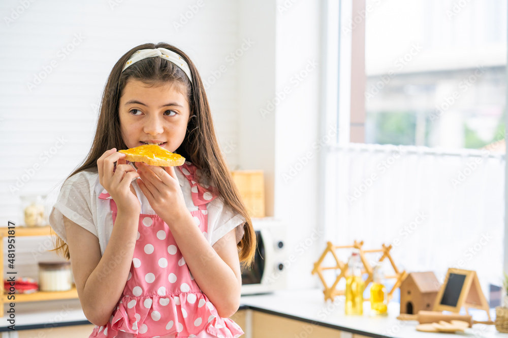 Young Caucasian girl wearing pajamas while put yam spread on the bread for breakfast inside of the modern kitchen. Lifestyle, healthy food concept. Young Caucasian girl wearing pajamas while put yam spread on the bread for breakfast inside of the modern kitchen. Lifestyle, healthy food concept.