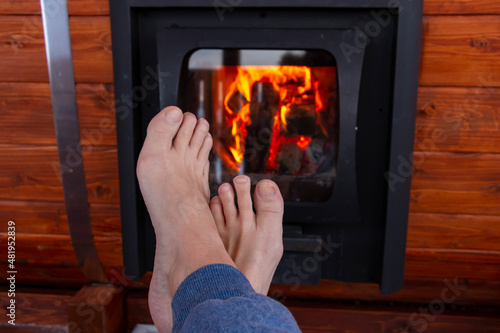 Legs without shoes by the fireplace. A woman relaxes by a warm fire and warms her frozen legs. Winter hardening meditation concept