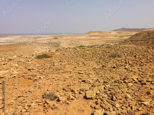 Bright lava rocks on Boa Vista Island, Cape Verde. Volcanic hills in the distance, dry arid climate, sandy terrain. Selective focus on the details, blurred background.