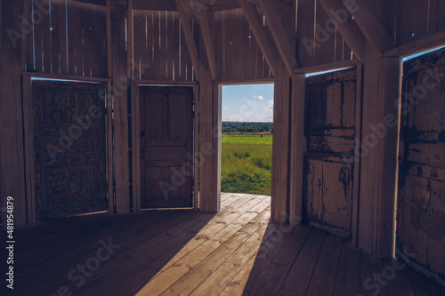 Inside white wooden Rotunda building with many doors with a view to a green meadow grass field © Olga
