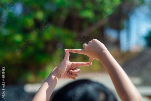 A little child is making her hand gestures a camera symbol to aim at a target like is actually using a camera.