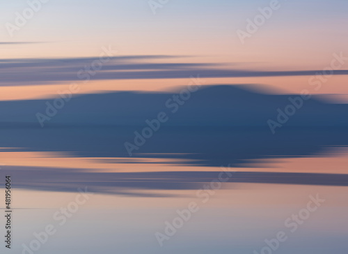 Intentional camera movement of sunset landscape image of distant mountains with pastel colors reflected in the calm ocean