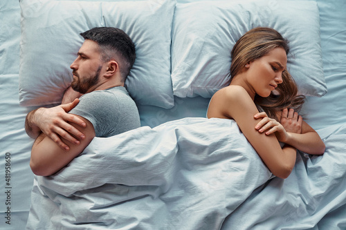 Fotobehang Young beautiful couple lying in bed turned back to back, arms crossed in anger and resentment
