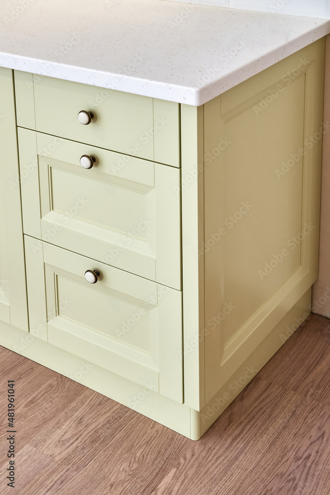 Fototapeta premium Classic chest of drawers with light green facades and acrylic solid surface countertop in light modern kitchen close view