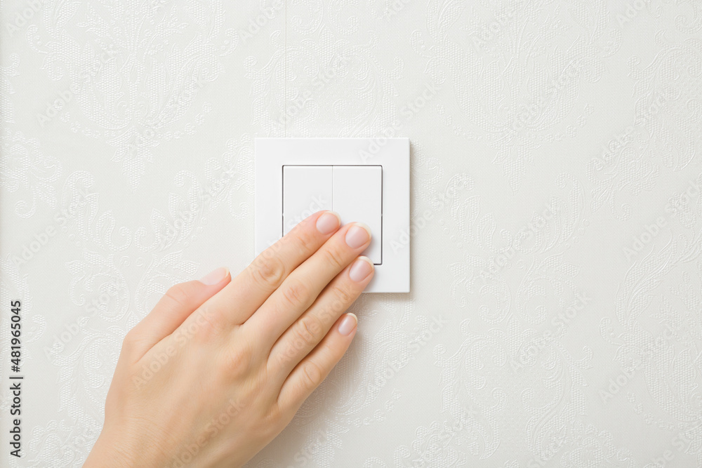 Young adult woman hand pressing white plastic light switch buttons at wall in room. Turn on or turn off lighting. Closeup. Energy saving at home. Young adult woman hand pressing white plastic light switch buttons at wall in room. Turn on or turn off lighting. Closeup. Energy saving at home.