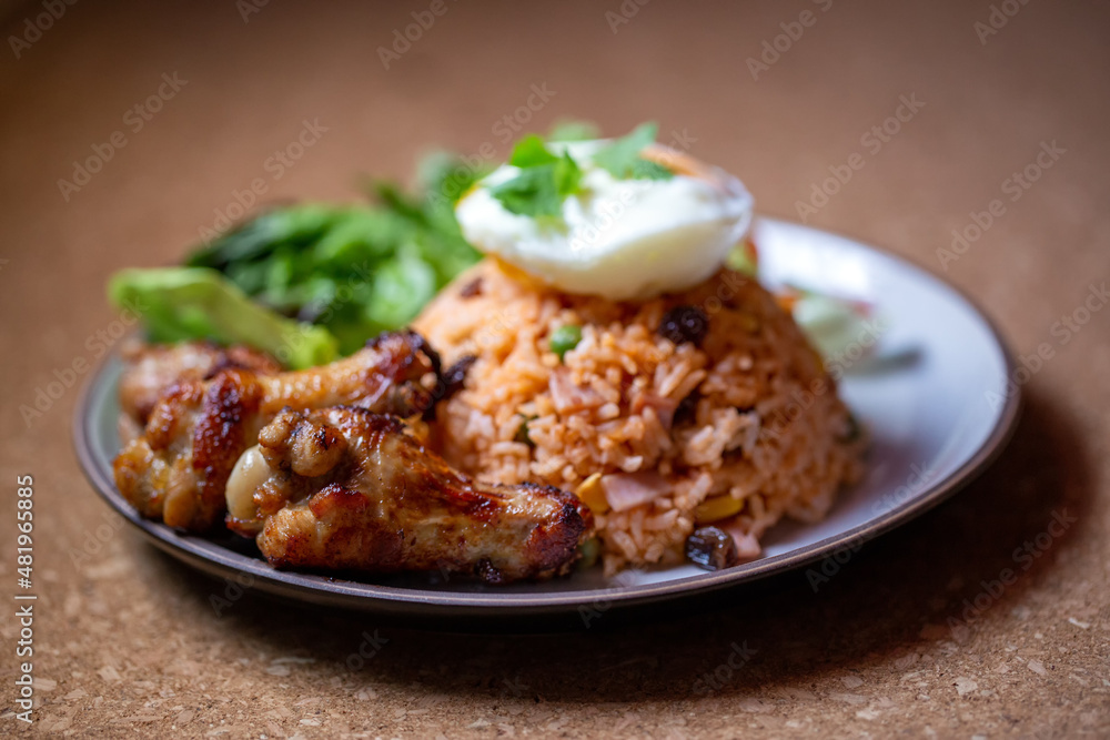 Close-up fried chicken in American fried rice dish, Thai traditional food fried rice mixed tomato sauce and grain with fried chicken, fresh vegetables, egg in side dishes. Close-up fried chicken in American fried rice dish, Thai traditional food fried rice mixed tomato sauce and grain with fried chicken, fresh vegetables, egg in side dishes.