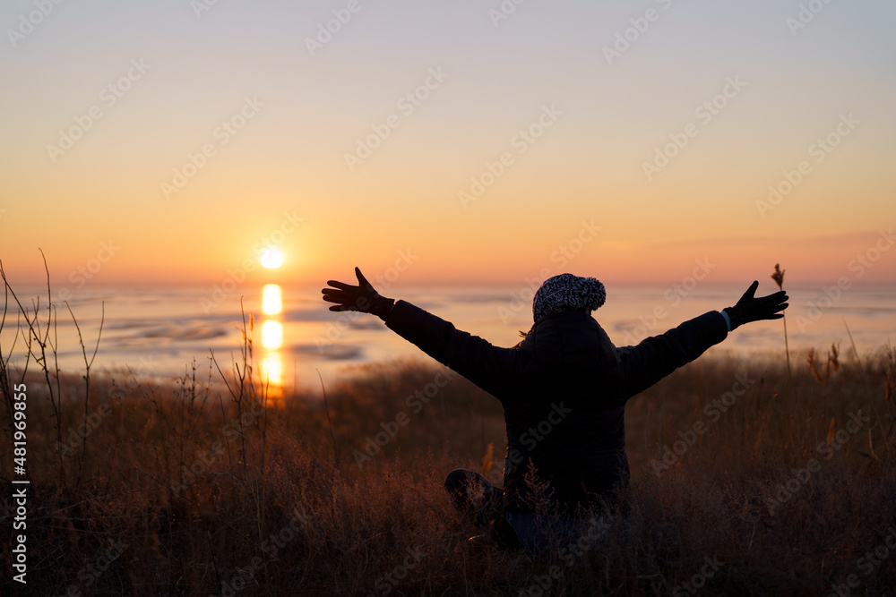 Woman silhouette with raised hand embracing the world on sunset. Freedom