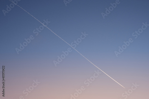 White diagonal aircraft trace on clear gradient evening sky after sunset. Plane trace.