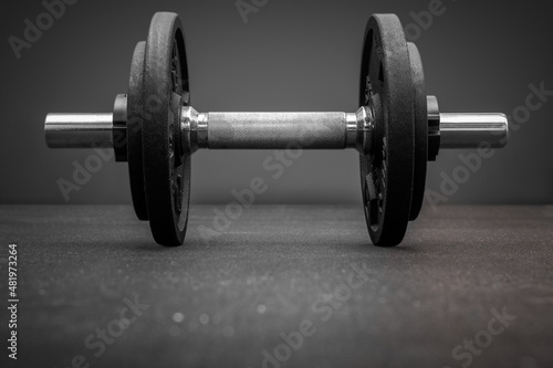 Black and white photo of dumbbell bar loaded with weight plates on the floor at the gym. Bodybuilding equipment on a clean background with copy space. Fitness, weight training or health concept