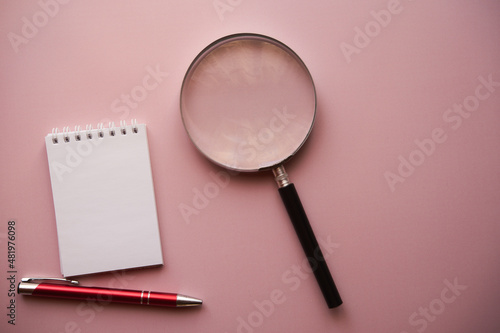 notes, lupa i długopis na różowym tle 