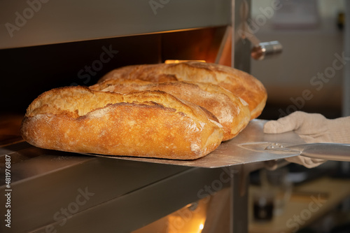 Close-up of a baker's shovel taking freshly baked artisan bread out of the oven. Bread production with copy space