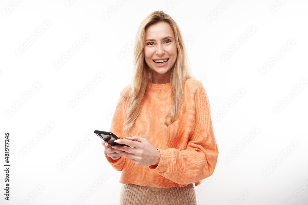 Beautiful blonde girl in casual looks at the smartphone screen and smiles isolated on white studio background Beautiful blonde girl in casual looks at the smartphone screen and smiles isolated on white studio background