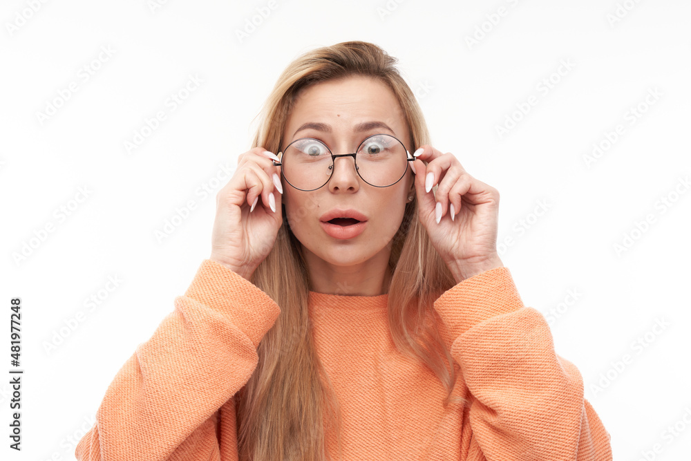 Shocked blond girl face with glasses looks surprised close-up on white studio background with copy space