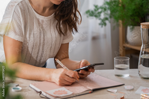 Woman holding a cell phone and plan Schedule Calendar, work online at home. Women hand planning daily appointment and note holiday trip in diary. 2022 Calendar reminder. Plan a week.