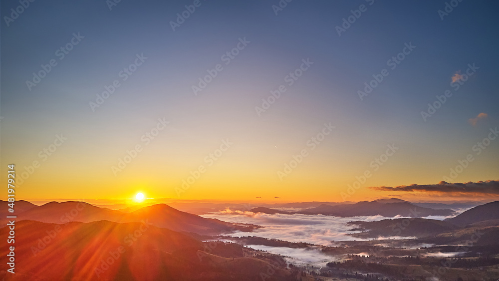 Colorful autumn sunrise over foggy woodland. Forest covered by low clouds. Fall rural landscape. Village in misty valley.