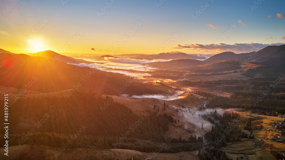 Colorful autumn sunrise over foggy woodland. Forest covered by low clouds. Fall rural landscape. Village in misty valley.