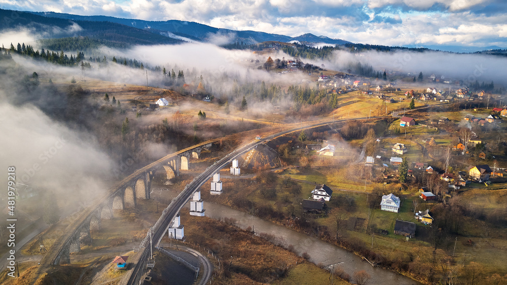 Autumn morning, foggy mountain valley. Railroad bridge, old viaduct in Vorohta. Village on hills covered by clouds. Fall rural landscape