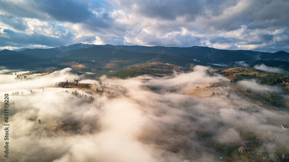 Colorful autumn morning over foggy mountain valley. Village covered by low clouds. Fall rural landscape. Misty cold November morning