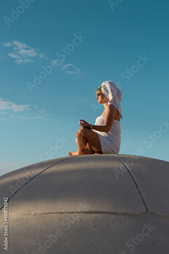 A woman in a towel meditating and greeting the morning on the roof of a spherical building.
