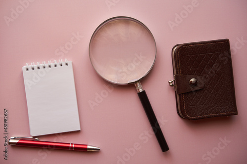 notes ,lupa długopis i brązowy portfel na różowym tle 