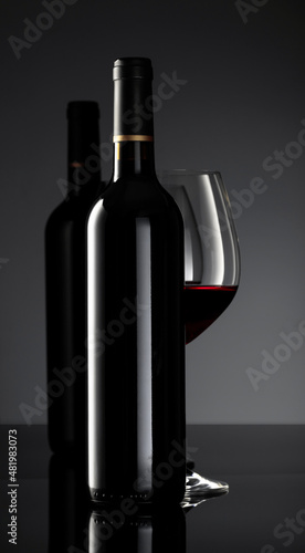 Bottle and glass of red wine on a black background.