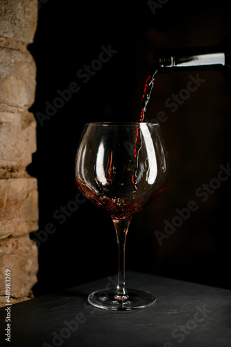 Close-up of stemware for burgundy wine into which red wine is poured from a bottle.