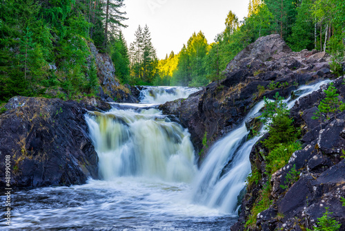 Beautiful landscape with waterfall in northern forest on summer evening. Powerful stream of water among stone rocks and green foliage. Kivach waterfall at Suna river in Karelia, Russia