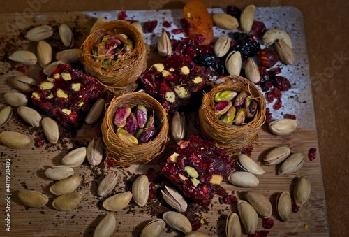 sweets with pistachios and dried fruits in baskets laid out on a wooden board on a brown background