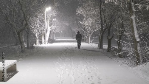man walks into the distance through the park on a winter night during a snowfall
