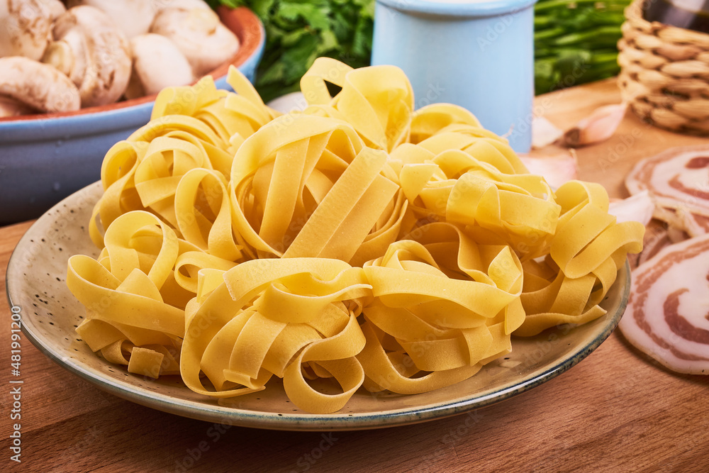 Traditional italian pasta - raw fettuccine nests in a plate on the kitchen table with ingredients for cooking pasta
