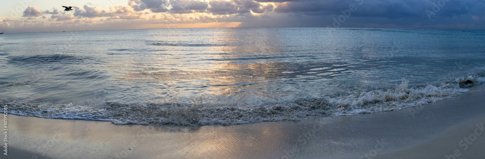 Panoramic photo of a warm Caribbean beach where turquoise waves splash you with water and together with the beautiful sky relax you and create a romantic and ideal atmosphere.