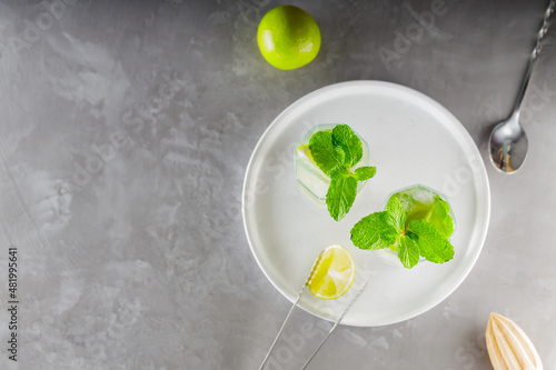 Mojito cocktail and bar accessories on gray background. Two highball glasses of mojito on a white plate. Summer refreshing cocktail with lime and mint. Copy space