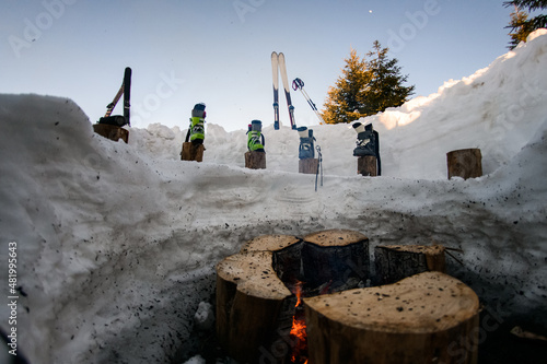 Fototapeta Naklejka Na Ścianę i Meble -  ski equipment and ski boots are in a row on wooden stumps near the fire