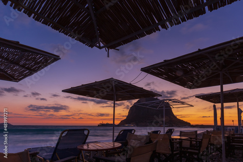 Beach cafe under straw umbrellas at colorful sunrise with silhouette of mountain  Monemvasia  Greece