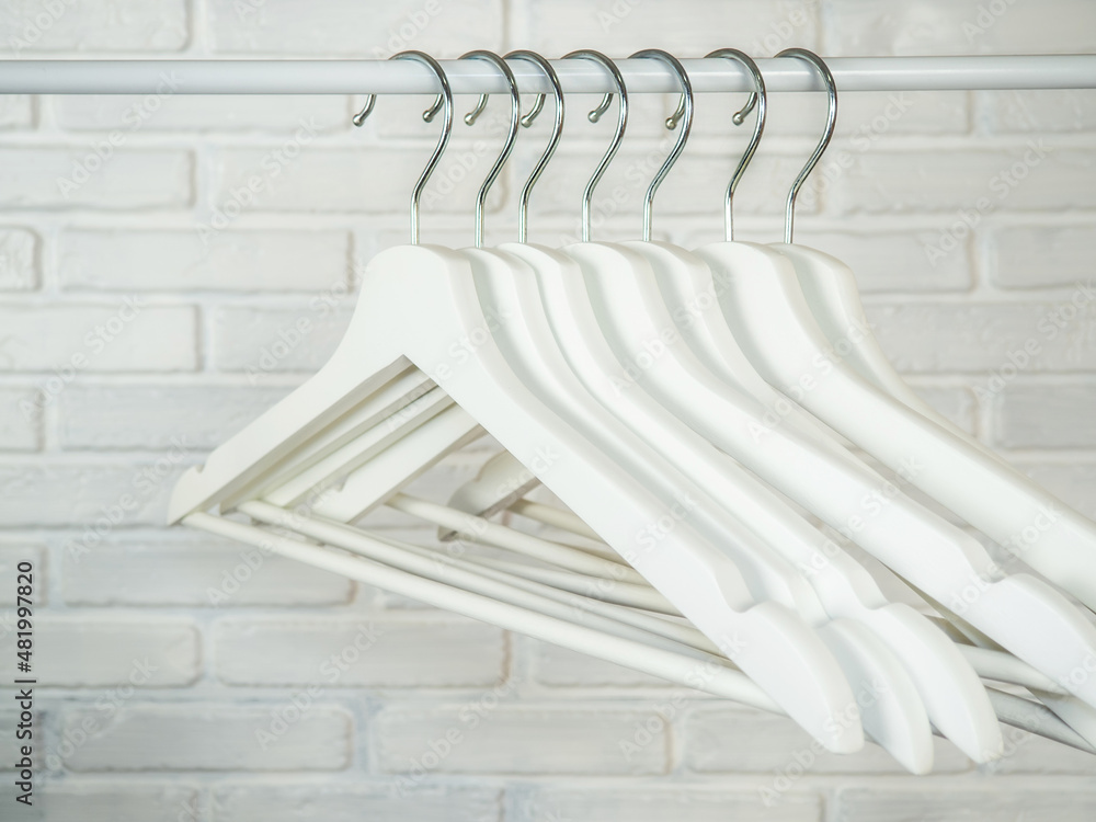 White hanger on a clothes rack with black hooks on a brick background.