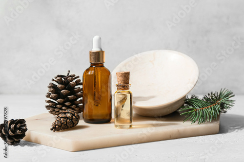 Composition with bottles of essential oil and cones on light background