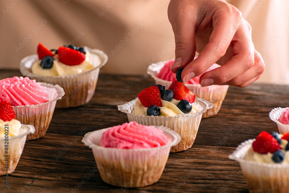 Pastry chef decorates the muffins with fresh berries. Cupcakes with strawberries and blueberries. Close up.