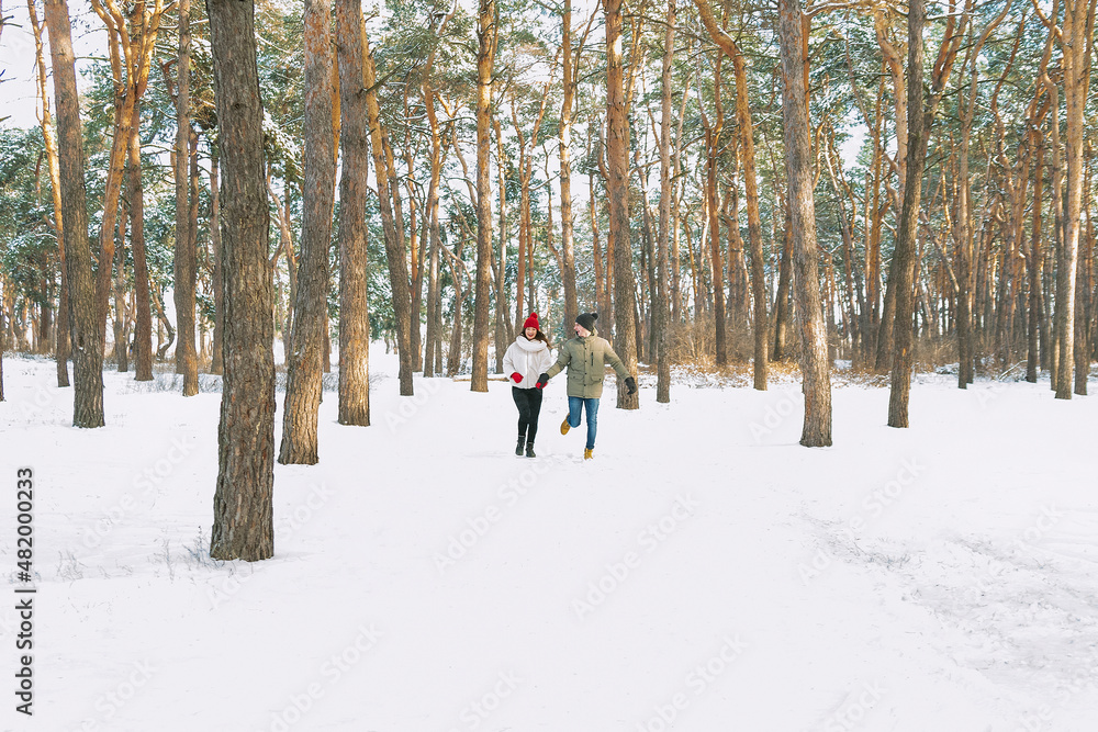 Young boy and girl running in winter park. Young couple are running on sunny day in snowy forest.