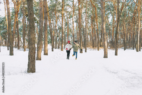Young boy and girl running in winter park. Young couple are running on sunny day in snowy forest.