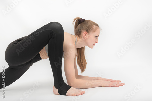 Young slender gymnast girl does an exercise to develop flexibility on white background. Asanas in yoga. Side view
