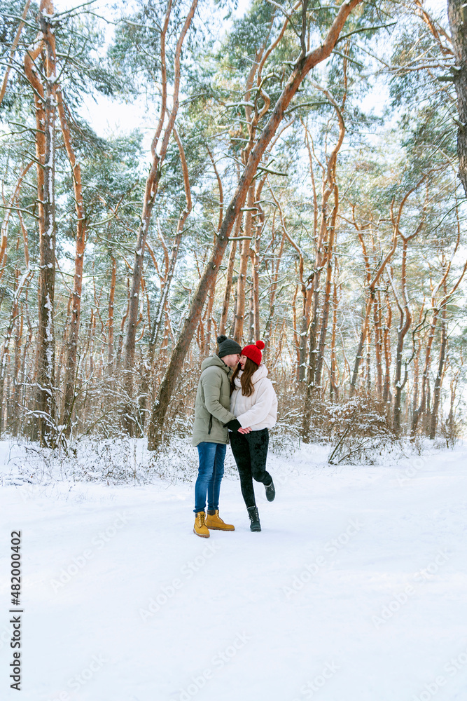 Couple in love walks through the winter forest and fools around. Vertical frame