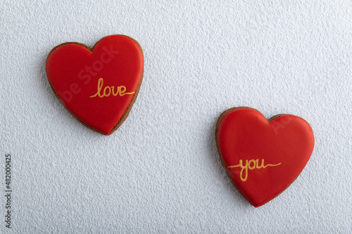 Two heart-shaped cookies with red sugar icing and inscription LOVE YOU, white background