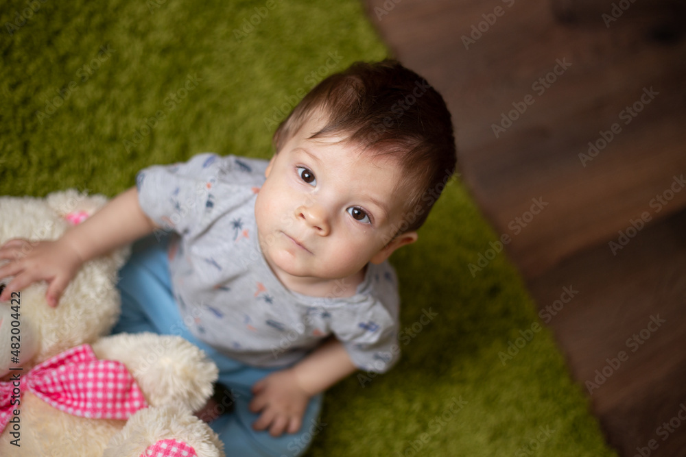 Beautiful little boy sitting on the floor. Baby toddler holds a Teddy bear