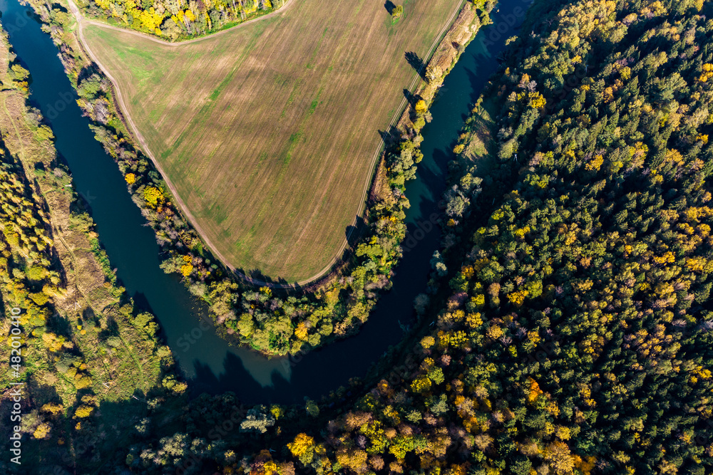 A sharp bend in a river that flows between forest and agricultural fields, aerial view