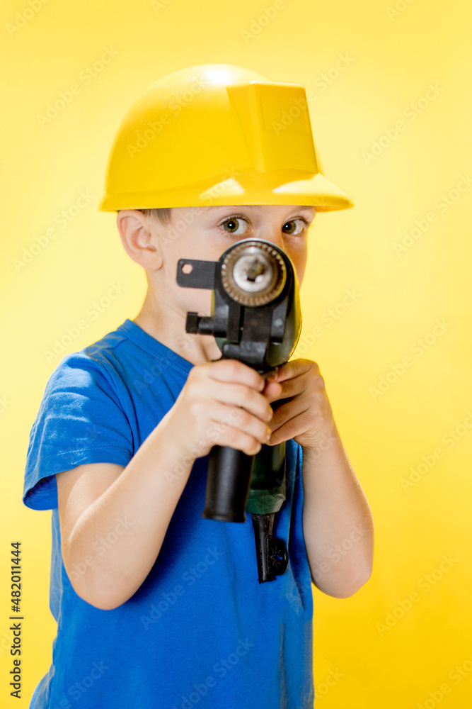 Cute boy in a construction helmet with a drill in his hands