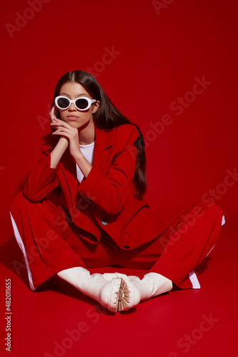 Fashion asian female model in red suit, white boots and sunglasses.