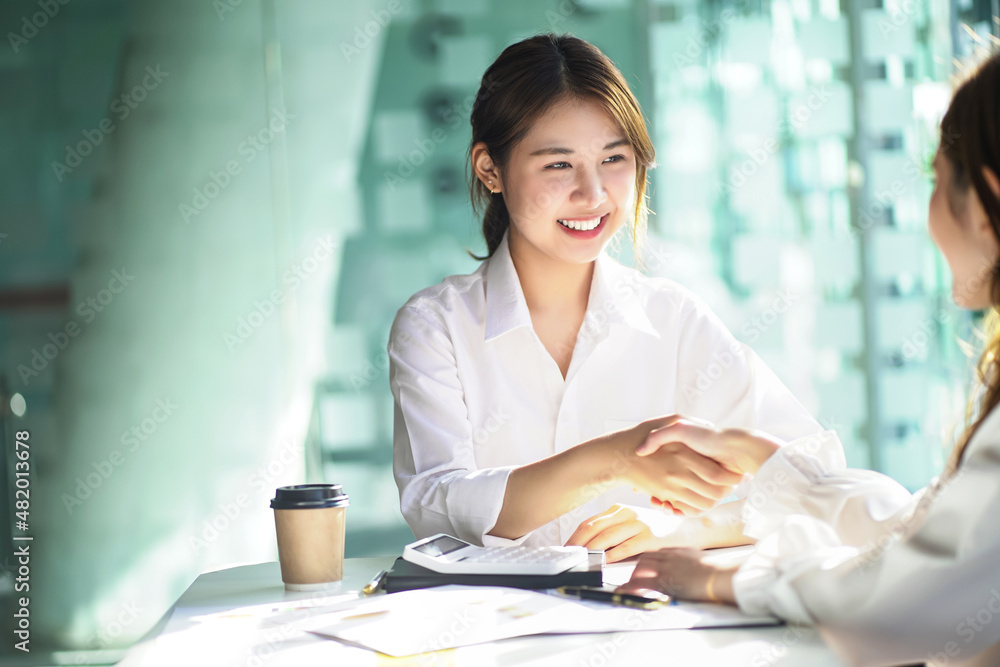 Asian business woman shakes hands in congratulations and looks at her colleague's face. Asian business woman shakes hands in congratulations and looks at her colleague's face.